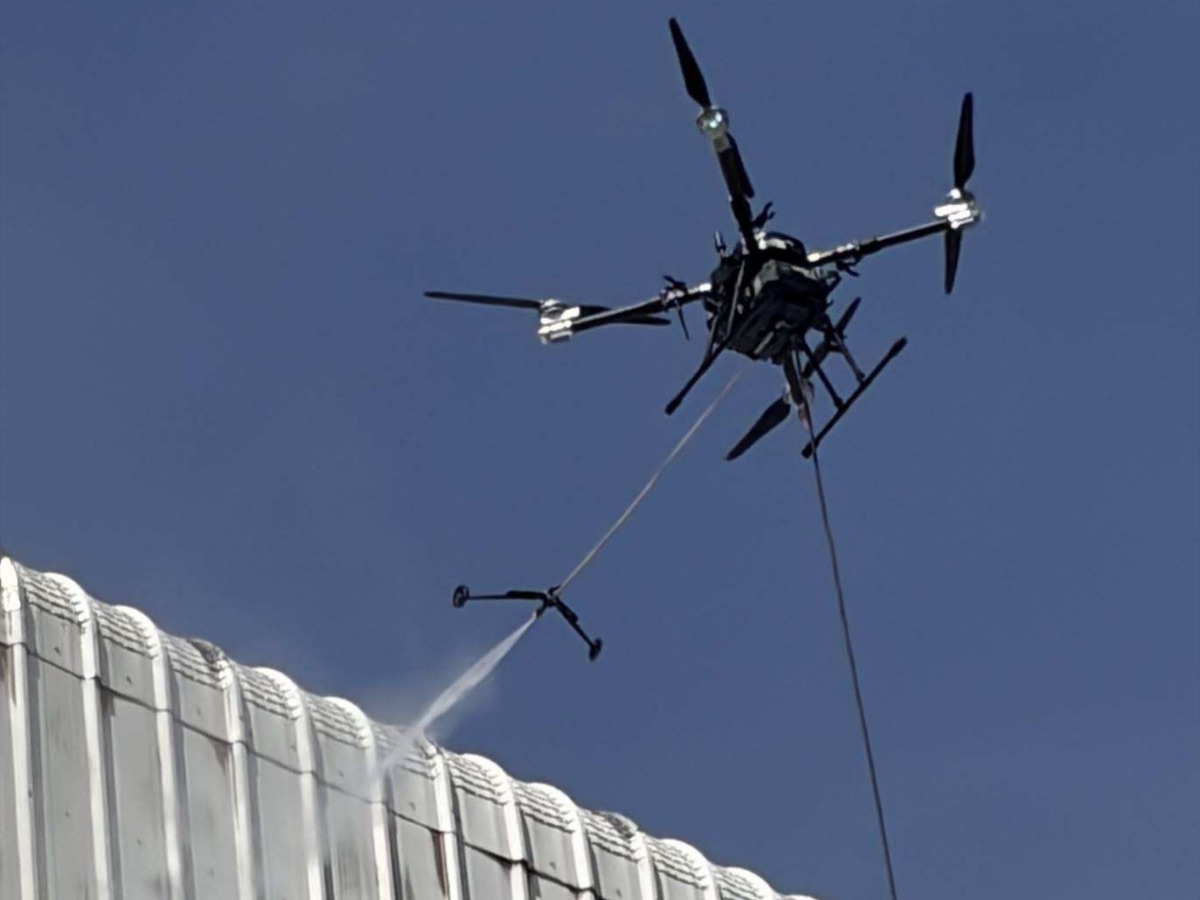 Drone lavando com jato de alta pressão a fachada metálica de um galpão industrial