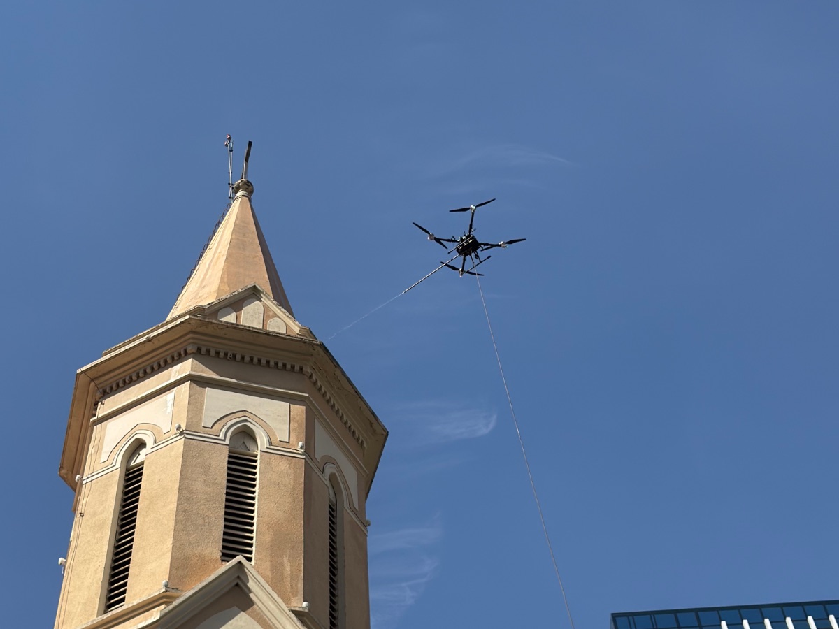 Drone lavando a torre de uma igreja histórica, com prédio espelhado ao fundo